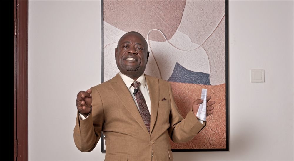 Kisuule Ben teaching in a brown suit